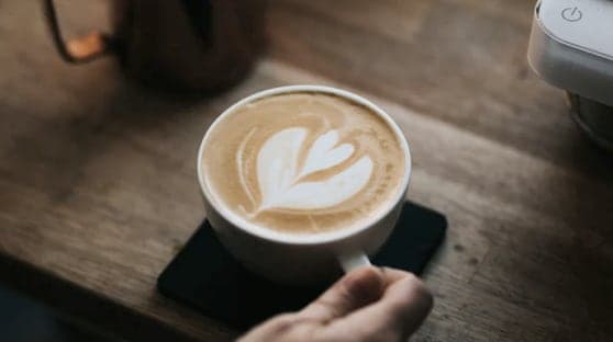 A coffee cup with latte art being grabbed by a hand